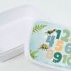 Auf dem Bild ist das Produkt: Brotdose mit Zahlen und Dinosauriern personalisiert mit Wunschnamen Schule Einschulungsgeschenk zum Preis von €16.90 abgebildet.