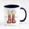 Auf dem Bild ist das Produkt: personalisierte Tasse mit Wanderstiefeln und Wildblumen Becher Geburtstagsgeschenk für einen Naturliebhaber mit Namen zum Preis von €17.90 abgebildet.
