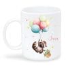 Auf dem Bild ist das Produkt: Tasse aus Keramik mit niedlichem Waschbär Motiv mit Korb und Luftballons, personalisiert mit Wunschnamen zum Preis von €16.9 abgebildet.