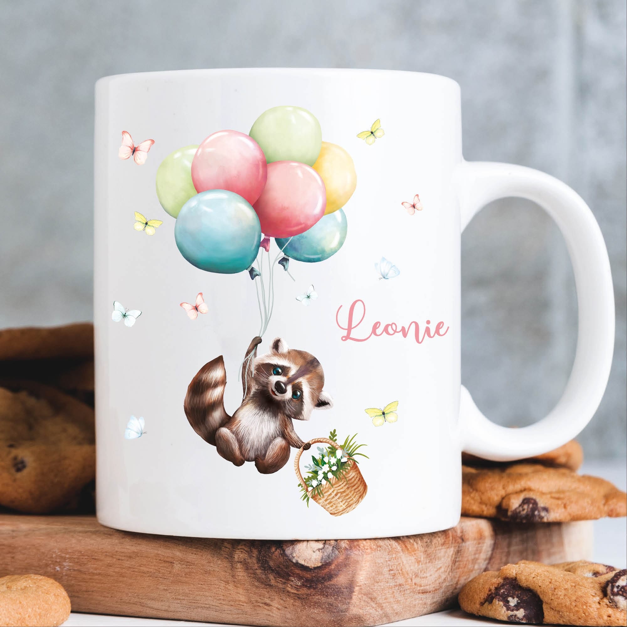 Tasse aus Keramik mit niedlichem Waschbär Motiv mit Korb und Luftballons, personalisiert mit Wunschnamen