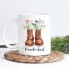 Auf dem Bild ist das Produkt: Tasse bedruckt mit Wanderstiefeln mit Wildblumen Gräsern und Wanderlust Kaffeetasse Geschenk zum Preis von €18.9 abgebildet.